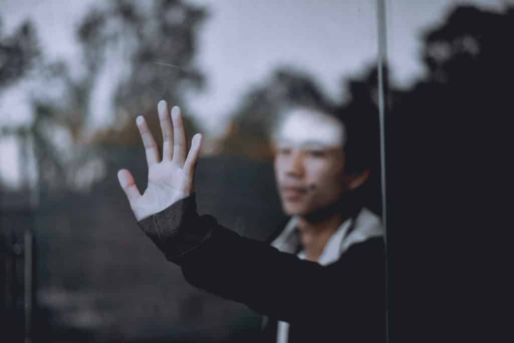 A depressed boy with his hand against the glass thinking